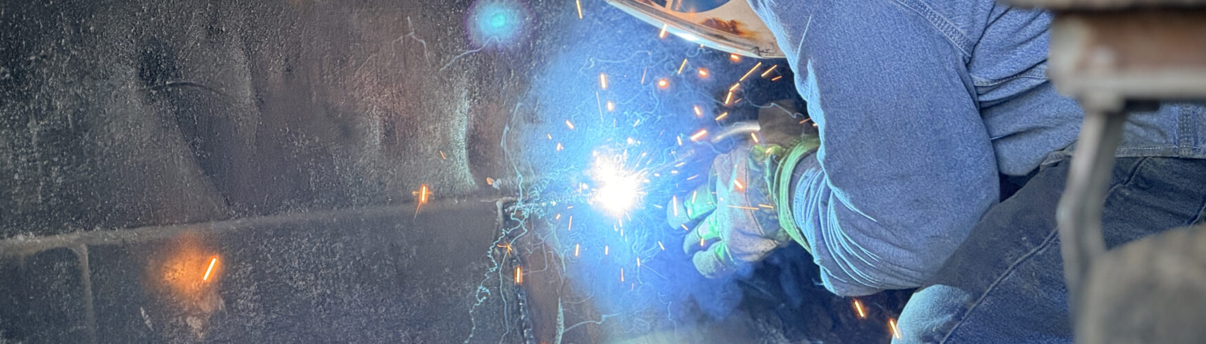 A man welding a patch on the wall of a truck with a welding hood with sparks